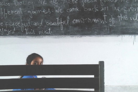 Shy girl in classroom hiding behind a chair