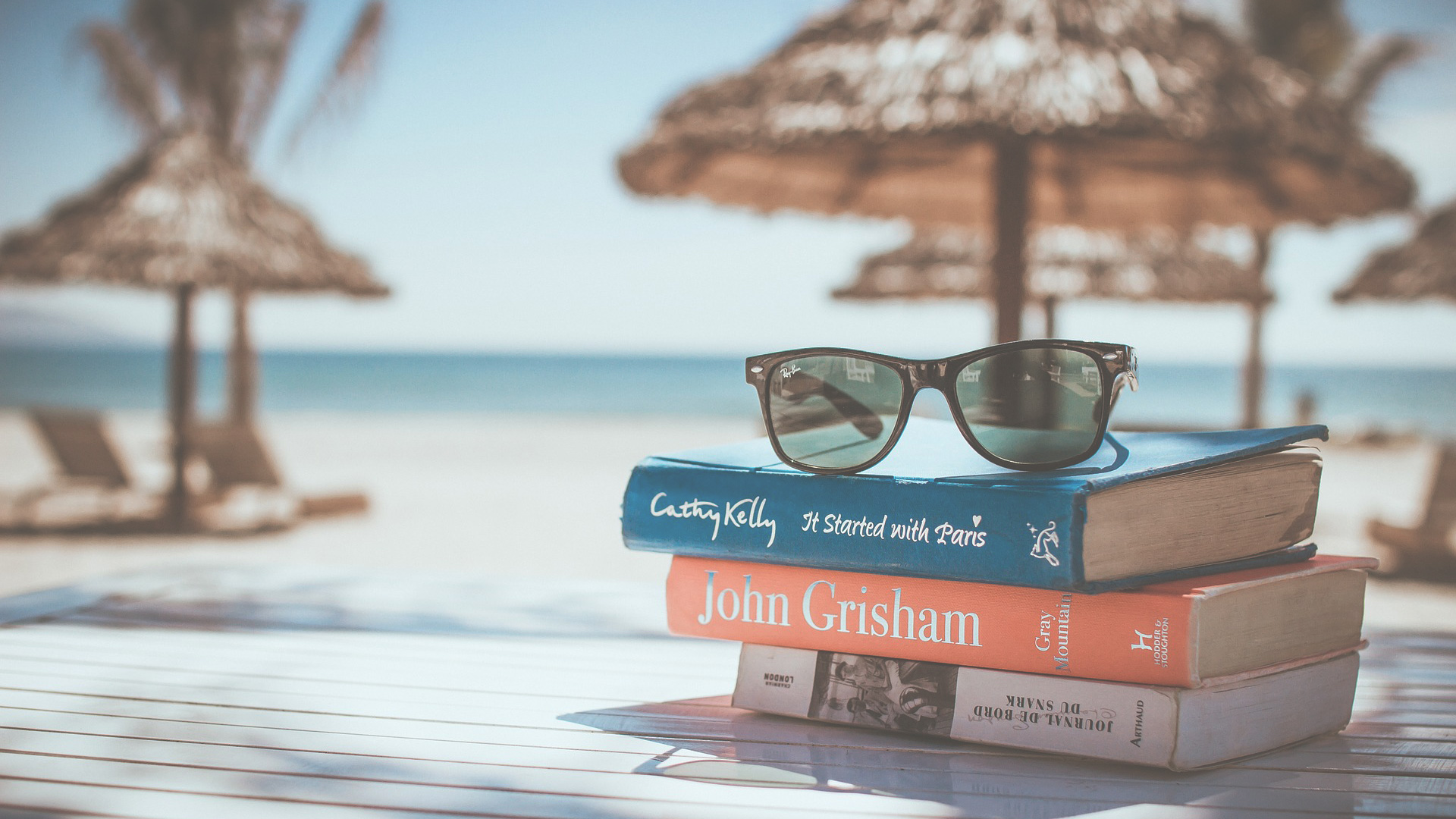 stack of books and glasses on a beach